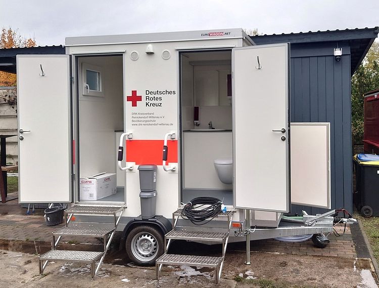 Sanitäranhänger der Bereitschaft steht mit geöffneten Türen auf einem Gelände