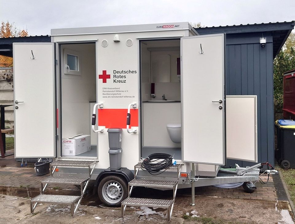 Sanitäranhänger der Bereitschaft steht mit geöffneten Türen auf einem Gelände